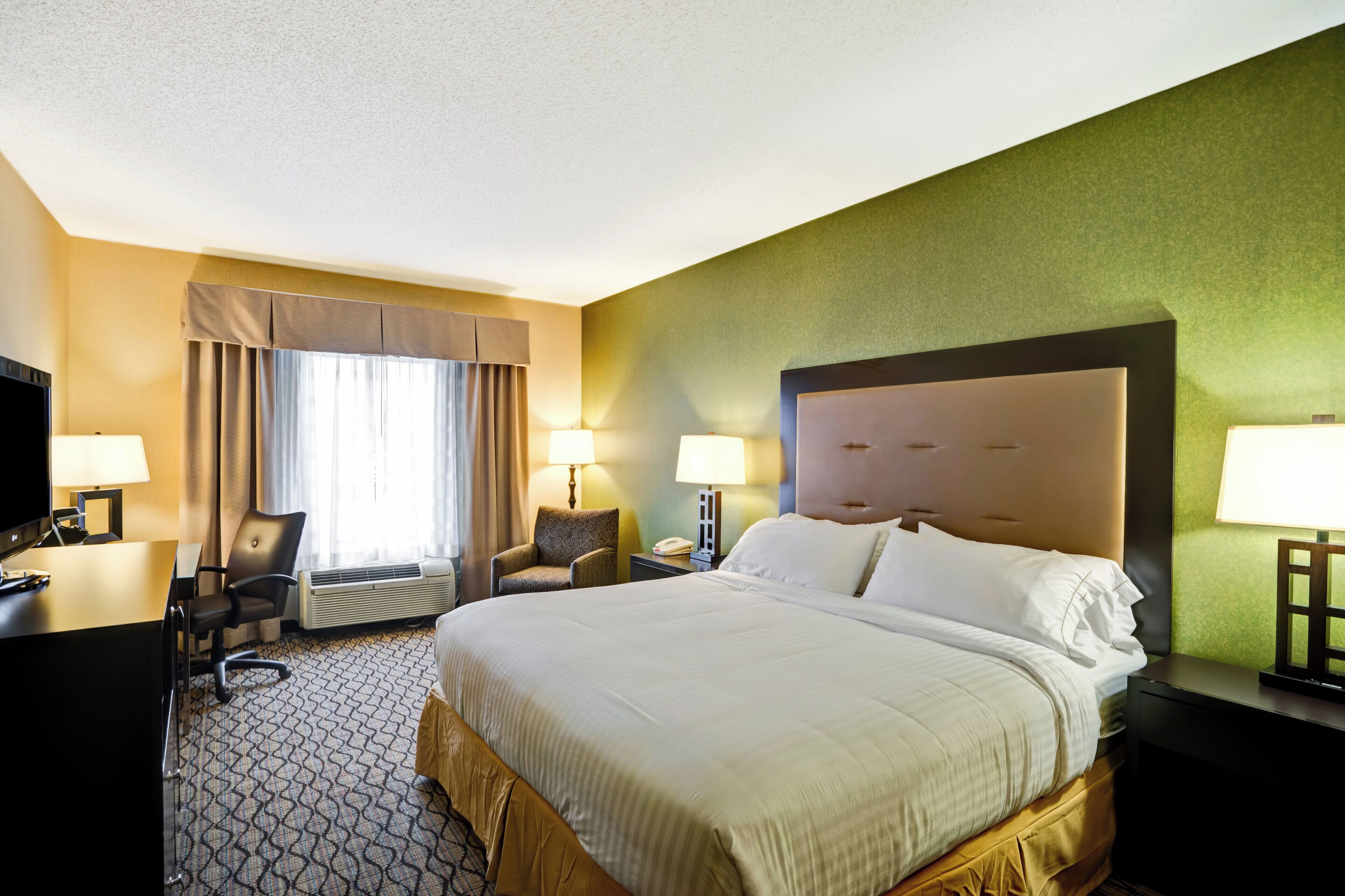 A hotel room with a large bed, two bedside lamps, a desk with a computer, a chair, and a television.