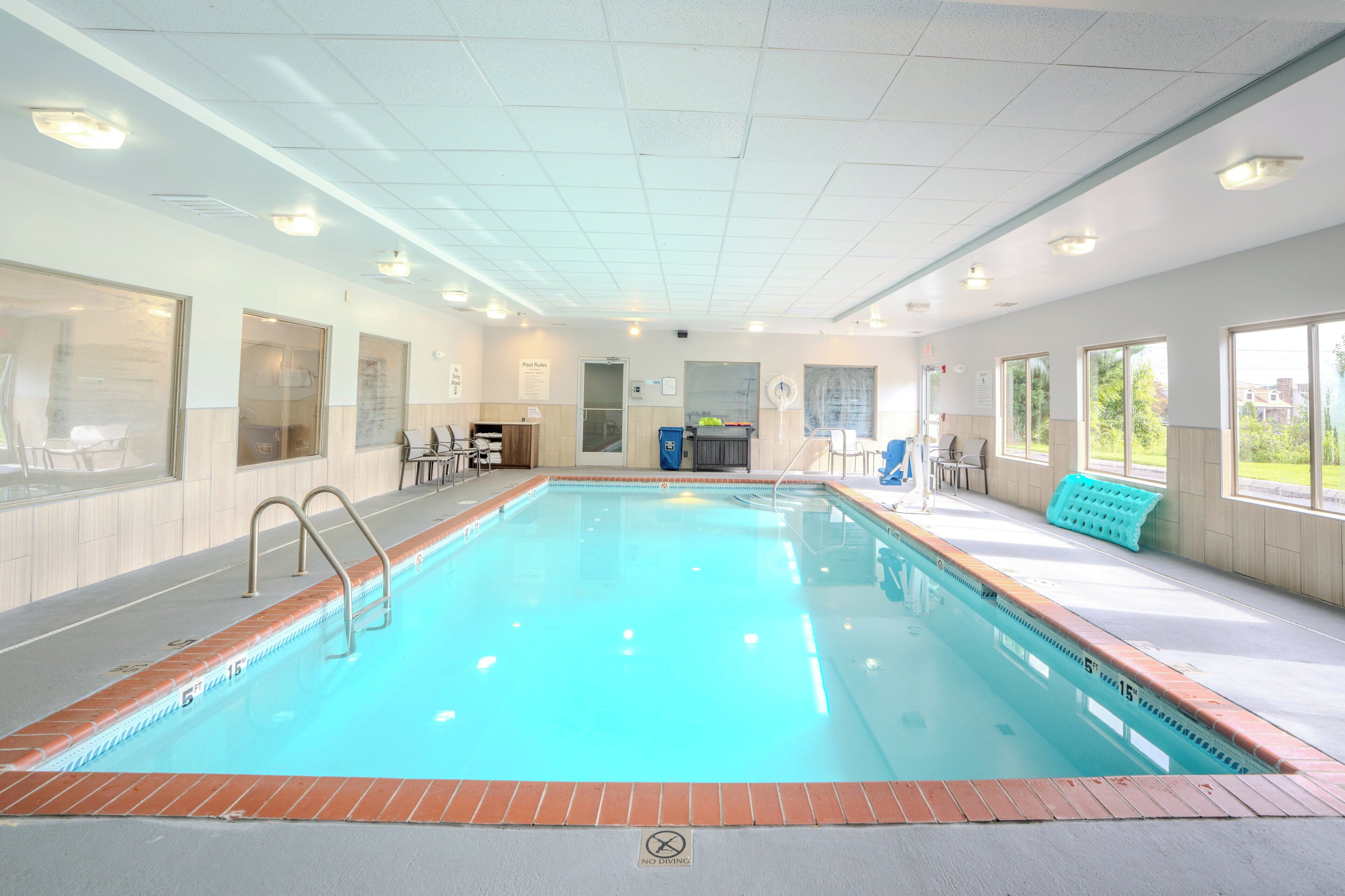Una piscina interior con agua cristalina, un cartel de prohibición de saltos y un cartel con las normas de la piscina.