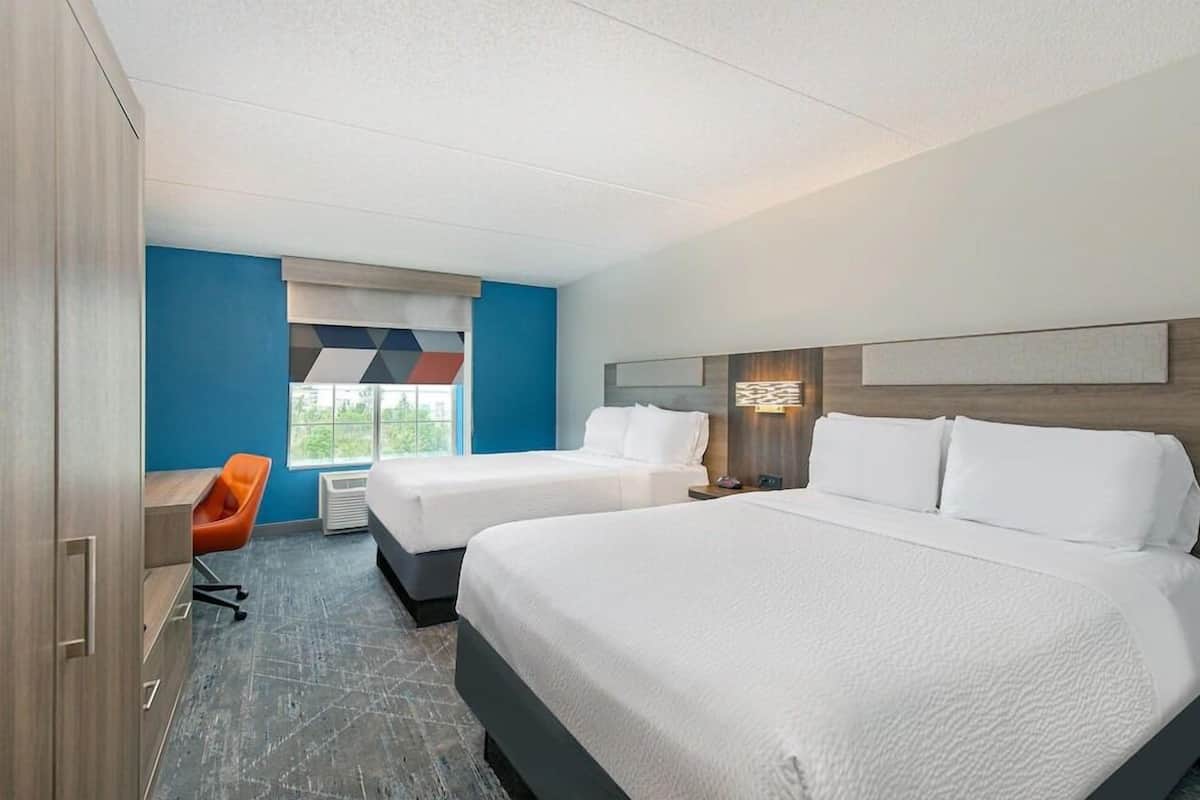 A hotel room with two beds, a desk, and a chair.