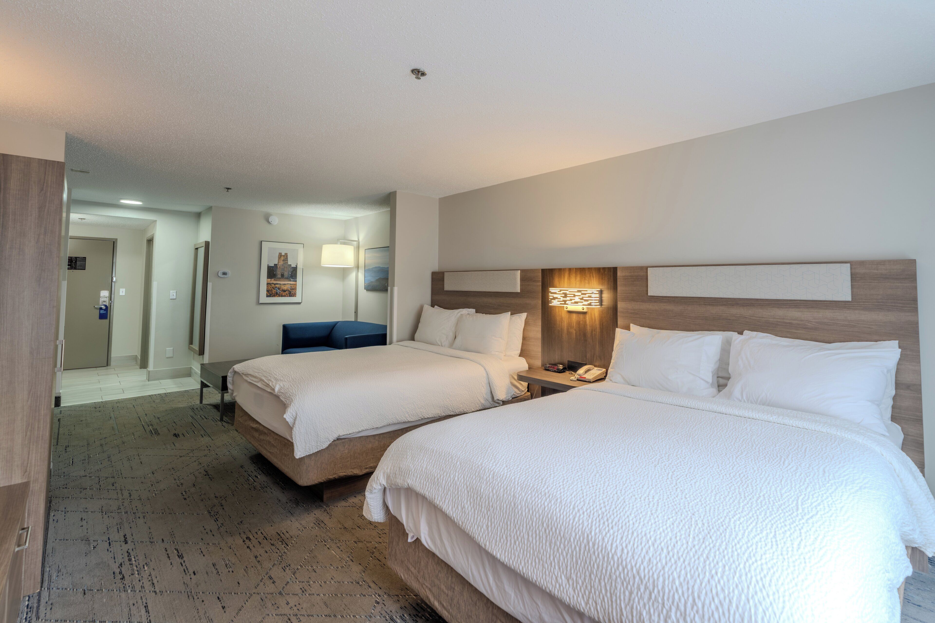 Habitación de hotel con dos camas, una mesita de noche con teléfono y una lámpara de pared.