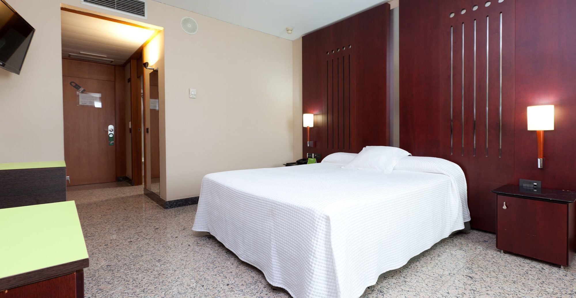 A hotel room with a bed, a desk, a wardrobe, and a door.