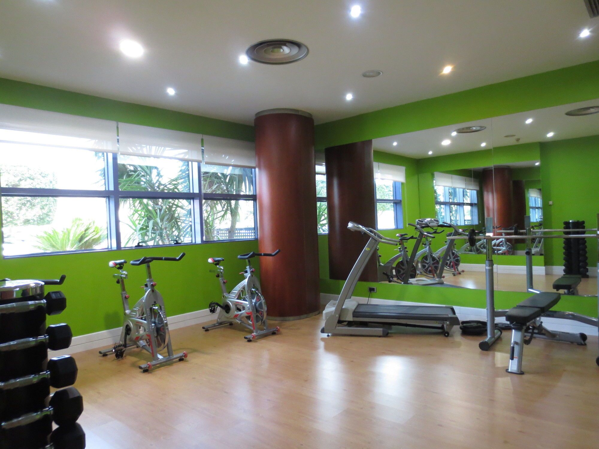 A gym with exercise equipment, large windows, and green walls.