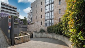A parking area with a curved concrete wall, a building with multiple windows, and a sign indicating a parking area. - Sercotel Cornella Barcelona (Cornella de Llobregat)