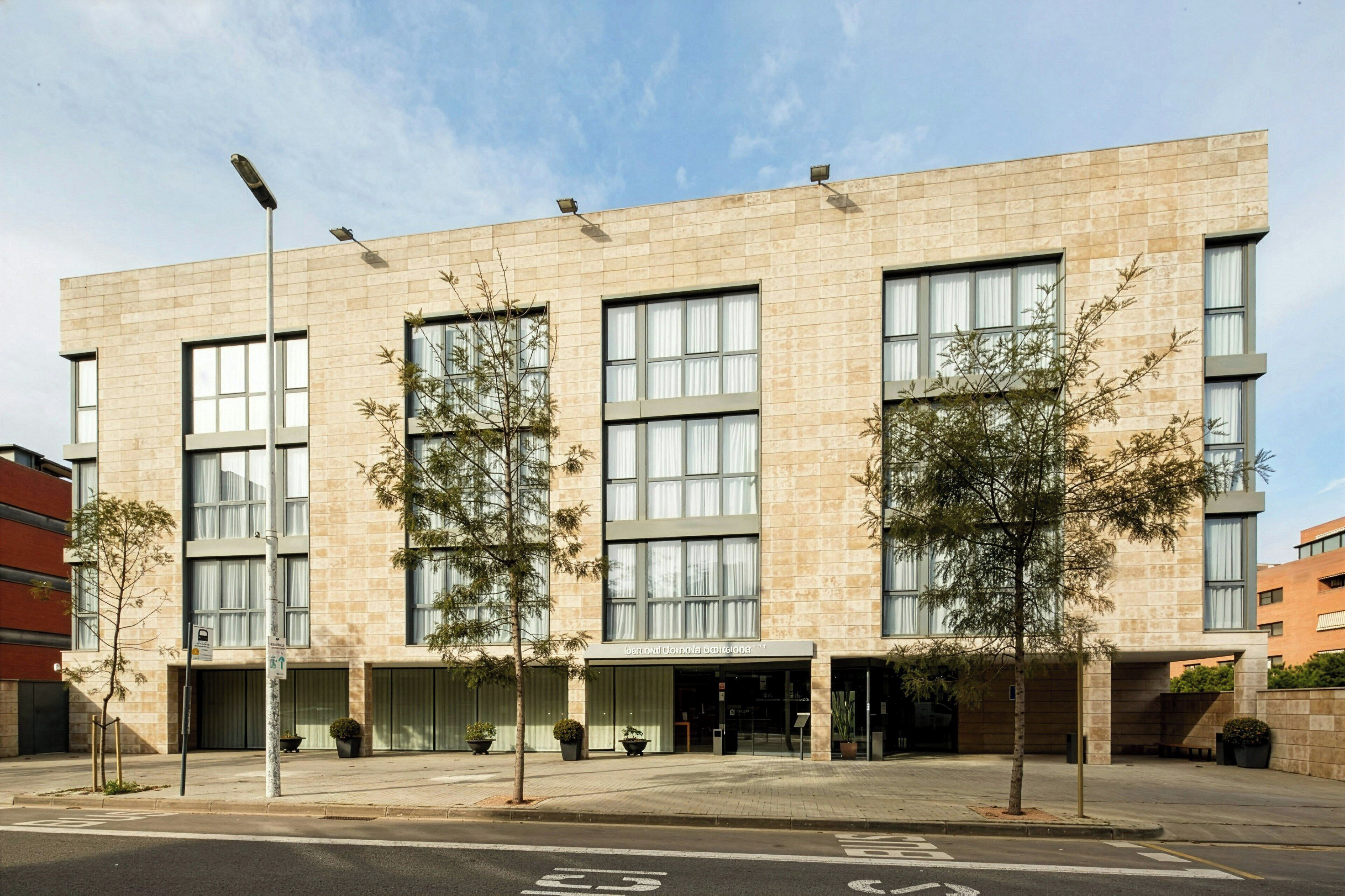 A modern building with large windows, a flat roof, and a paved entrance area with potted plants.