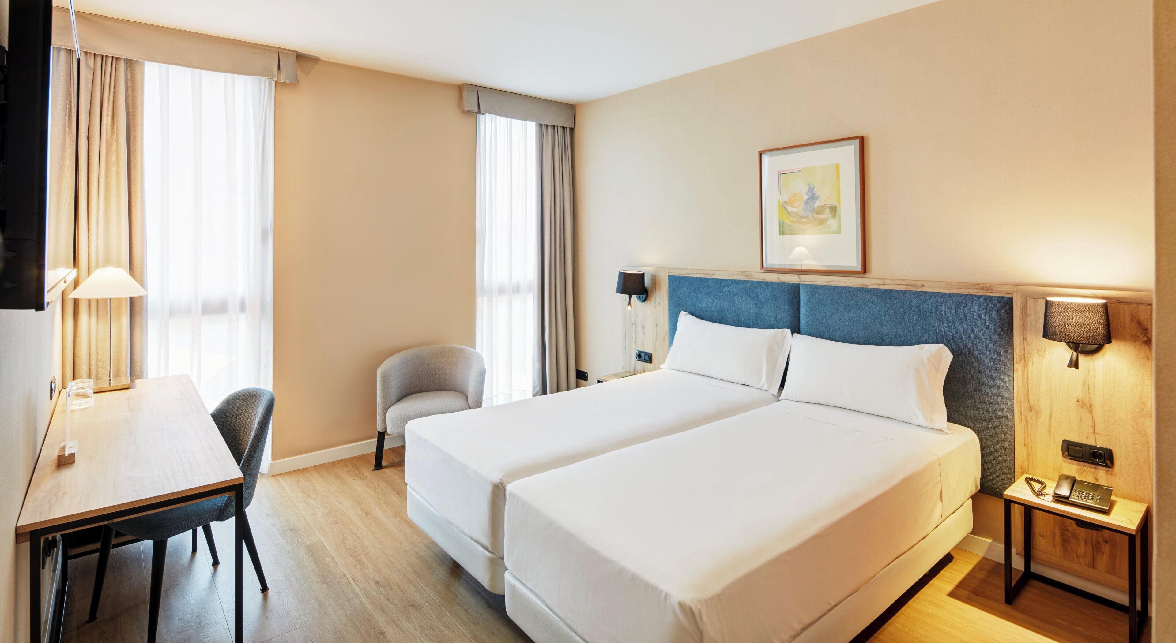 Ein Hotelzimmer mit zwei Betten, einem Schreibtisch, einem Stuhl, einer Lampe und einem Bild an der Wand.