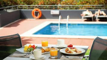 A dining table with breakfast items, a pool, and a lifebuoy in the background.