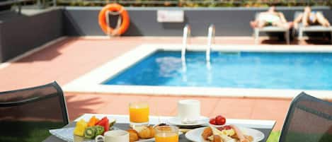 Una mesa de comedor con alimentos para el desayuno, una piscina y un flotador de seguridad al fondo.