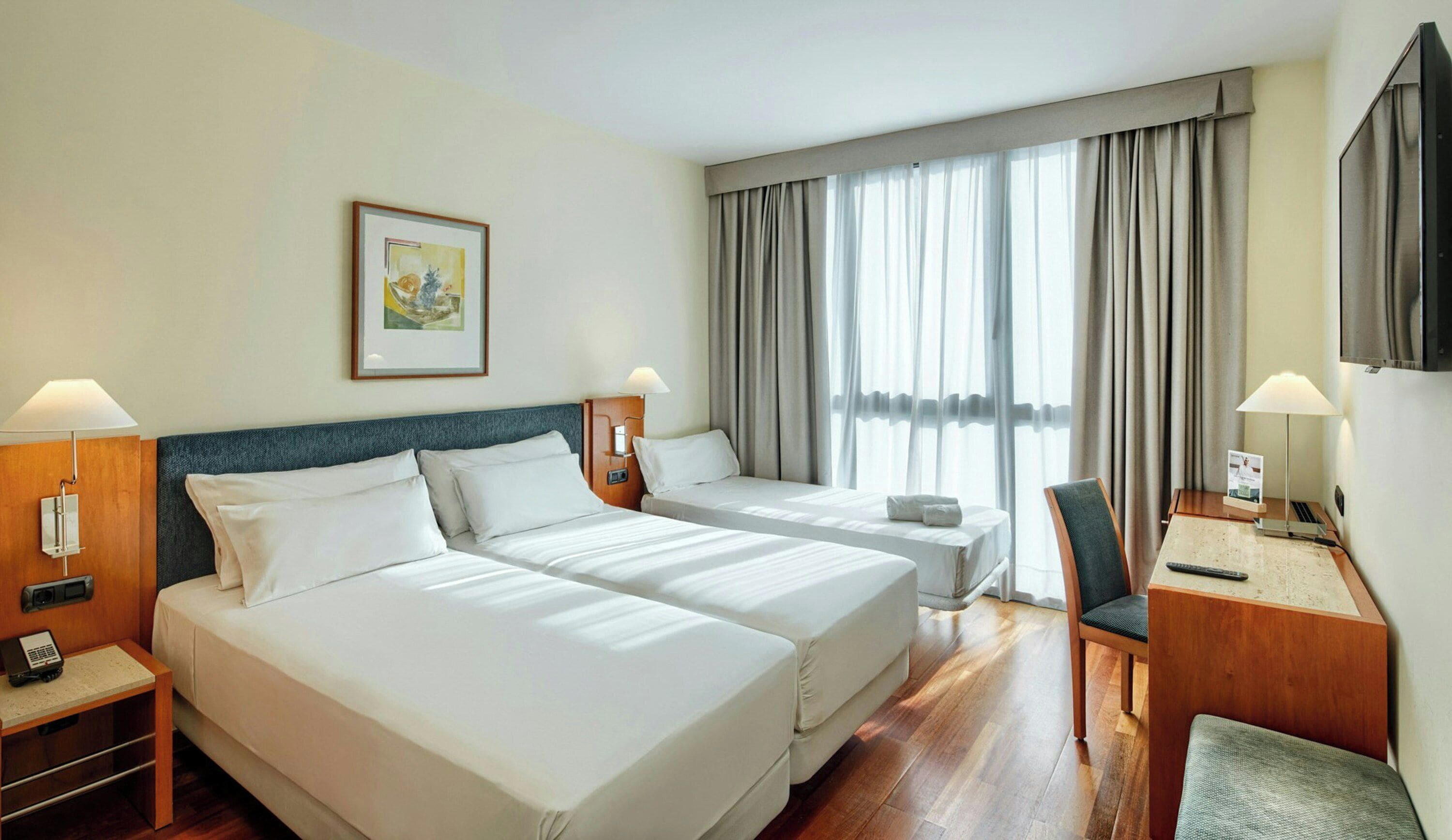 Une chambre d’hôtel avec deux lits, un bureau, une chaise, une télévision et un tableau au mur.
