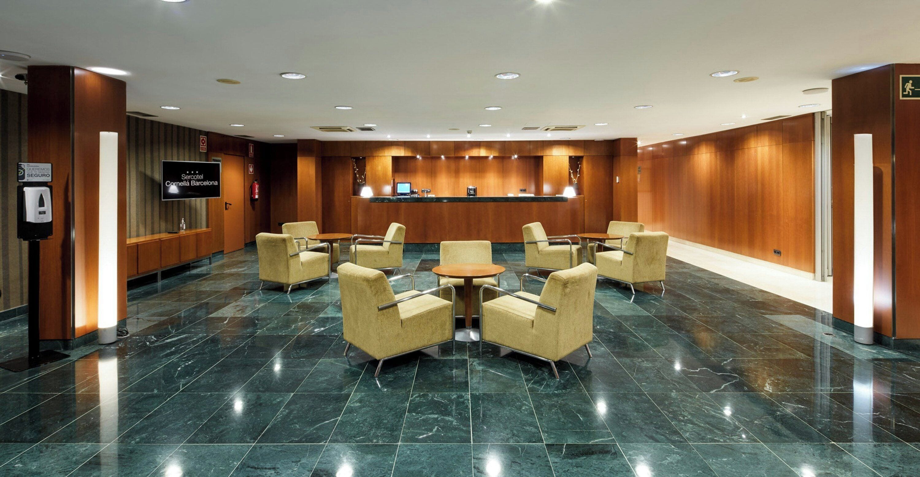 A hotel lobby with a reception desk, seating area, and a television screen.