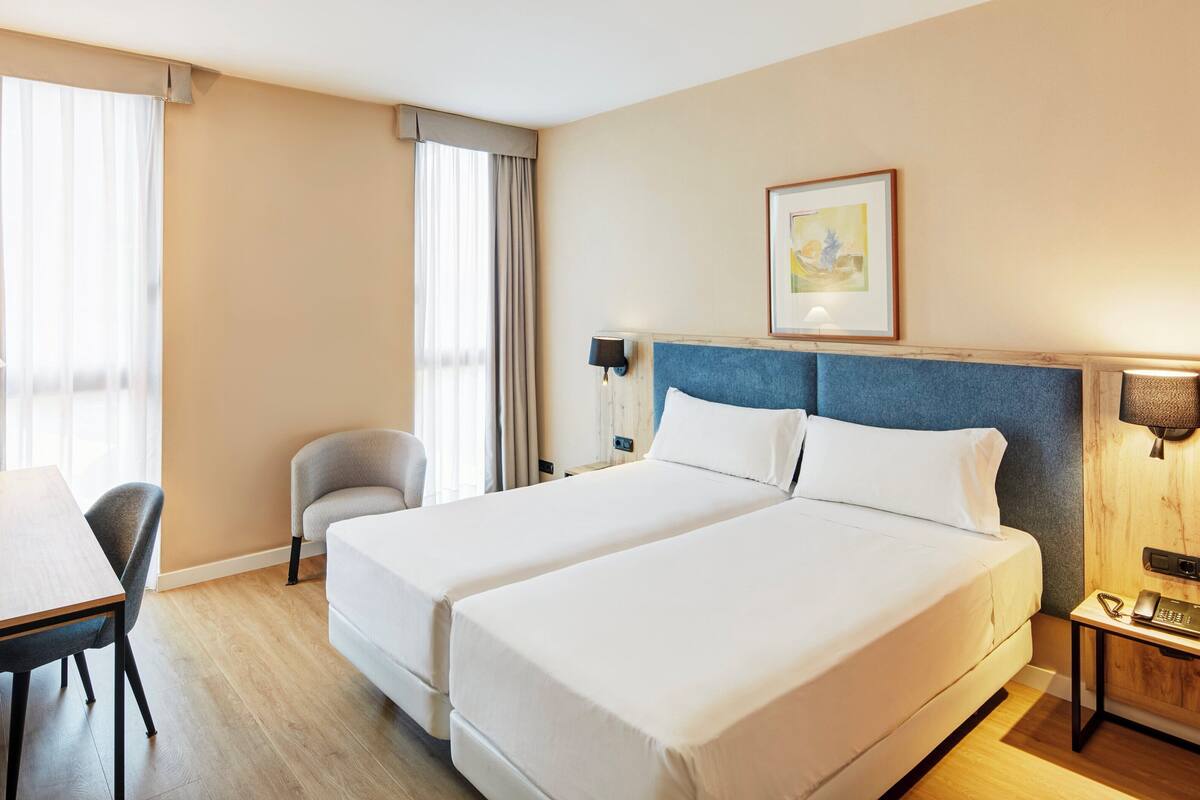 Habitació d'hotel amb dos llits, un escriptori, una cadira, una làmpada i un quadre a la paret.