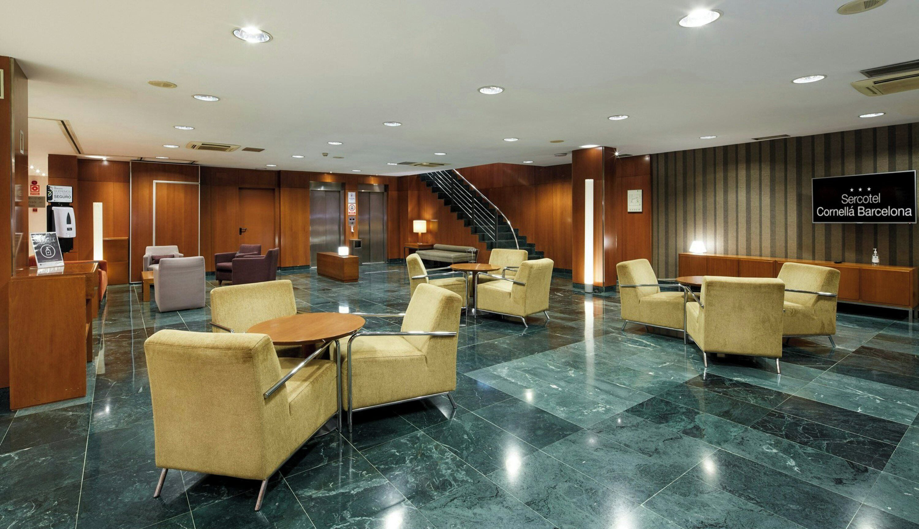 Un vestíbulo de hotel con mostrador de recepción, zona de estar y una escalera.