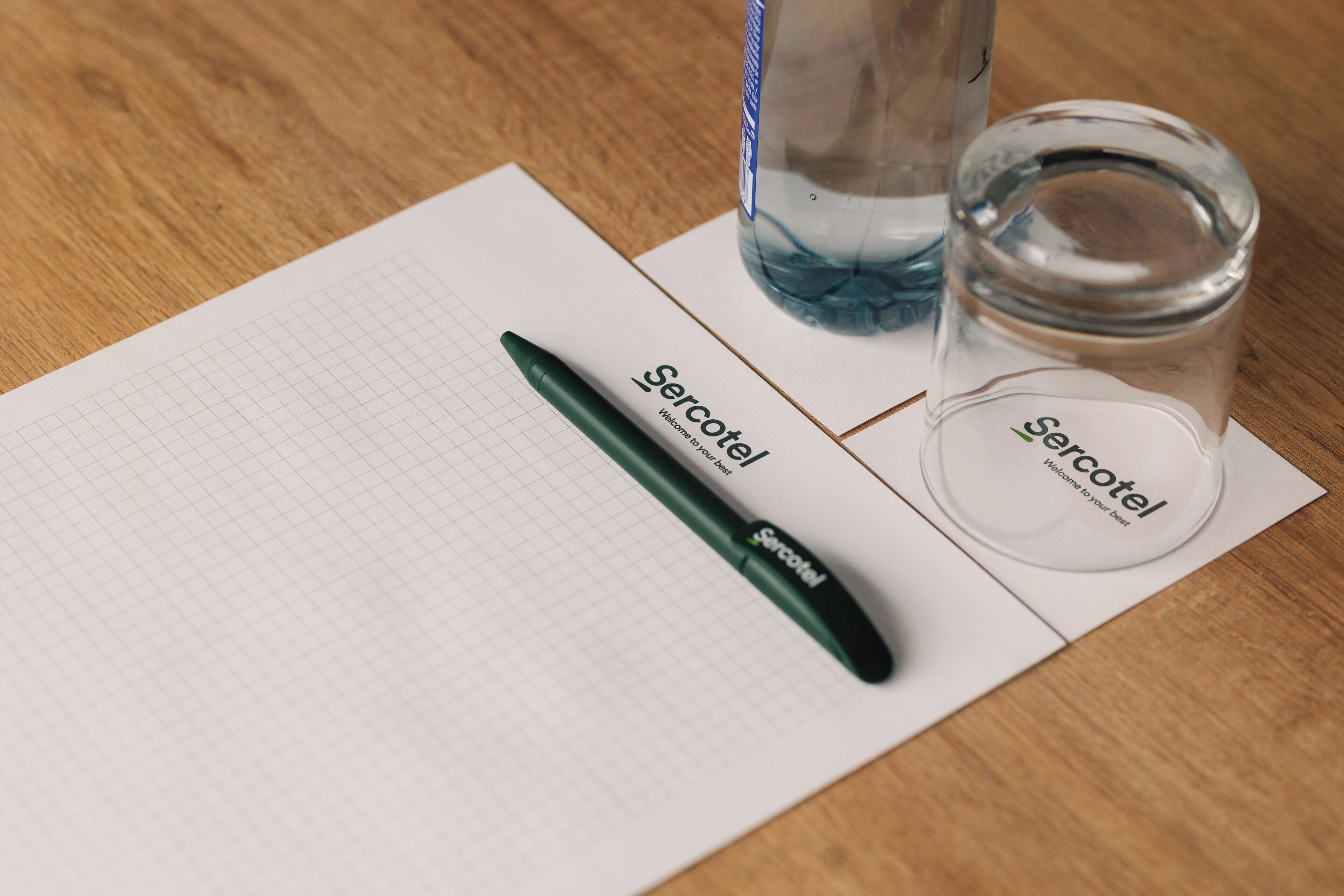 Un cuaderno de cuadrícula, un bolígrafo verde, una botella de vidrio y un frasco de vidrio sobre una mesa de madera.