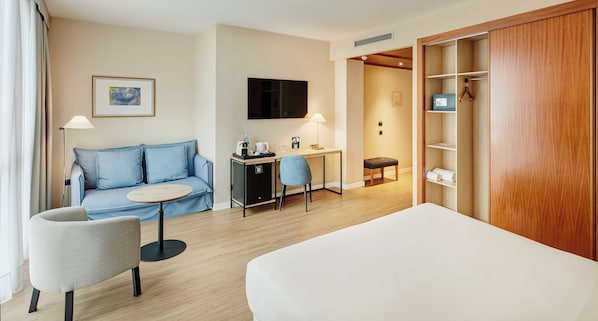 A hotel room with a bed, a sofa, a desk, a chair, a TV, and a wardrobe.