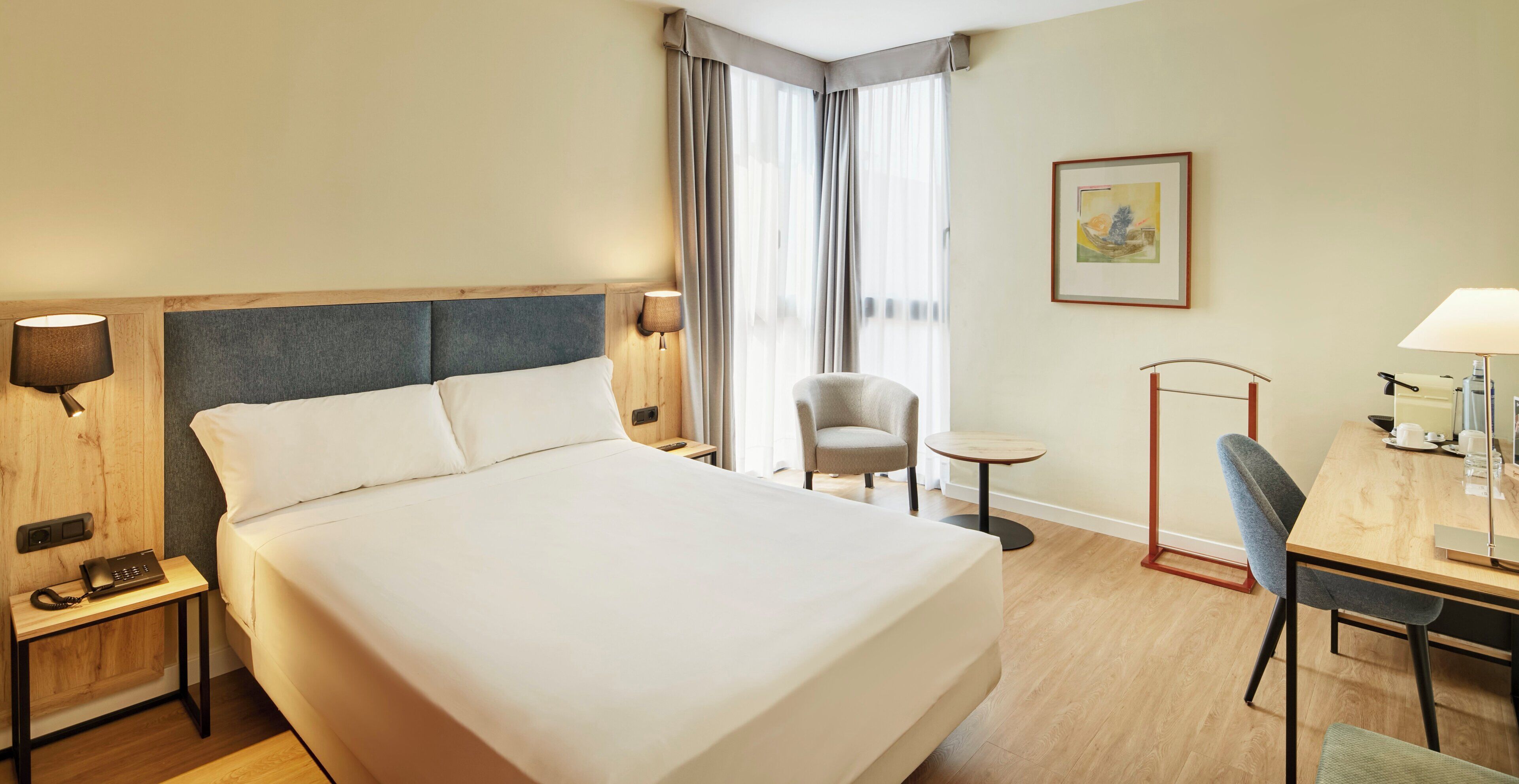 A hotel room with a large bed, bedside tables, a desk with a chair, a small table, and a lamp.