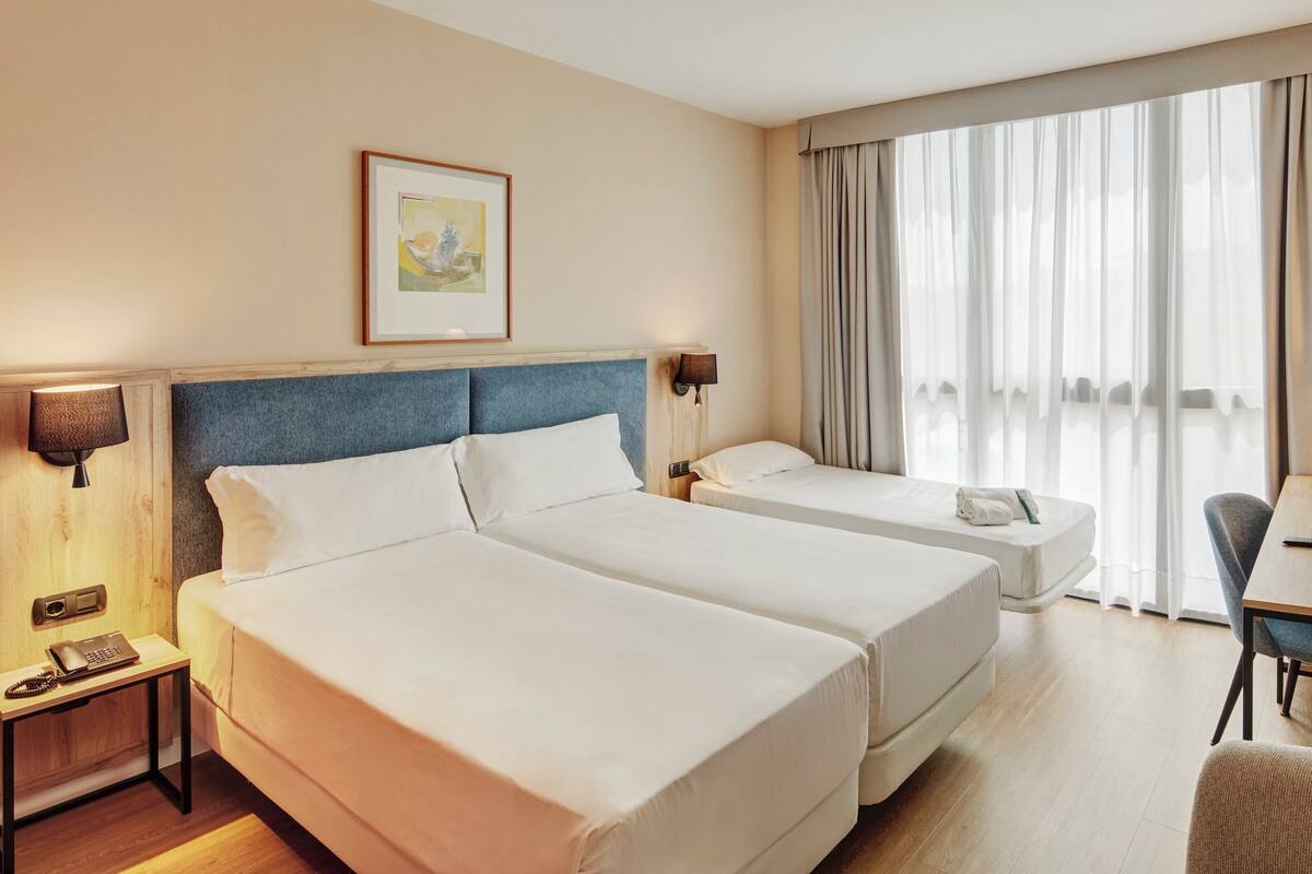 A hotel room with two beds, a desk, a chair, a lamp, and a framed picture on the wall.