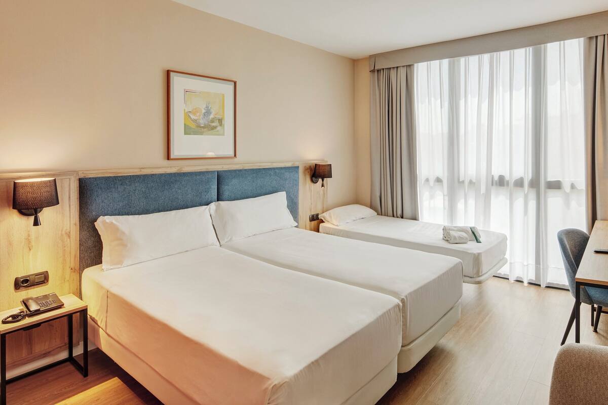 Habitació d'hotel amb dos llits, escriptori, cadira, làmpada i un quadre a la paret.