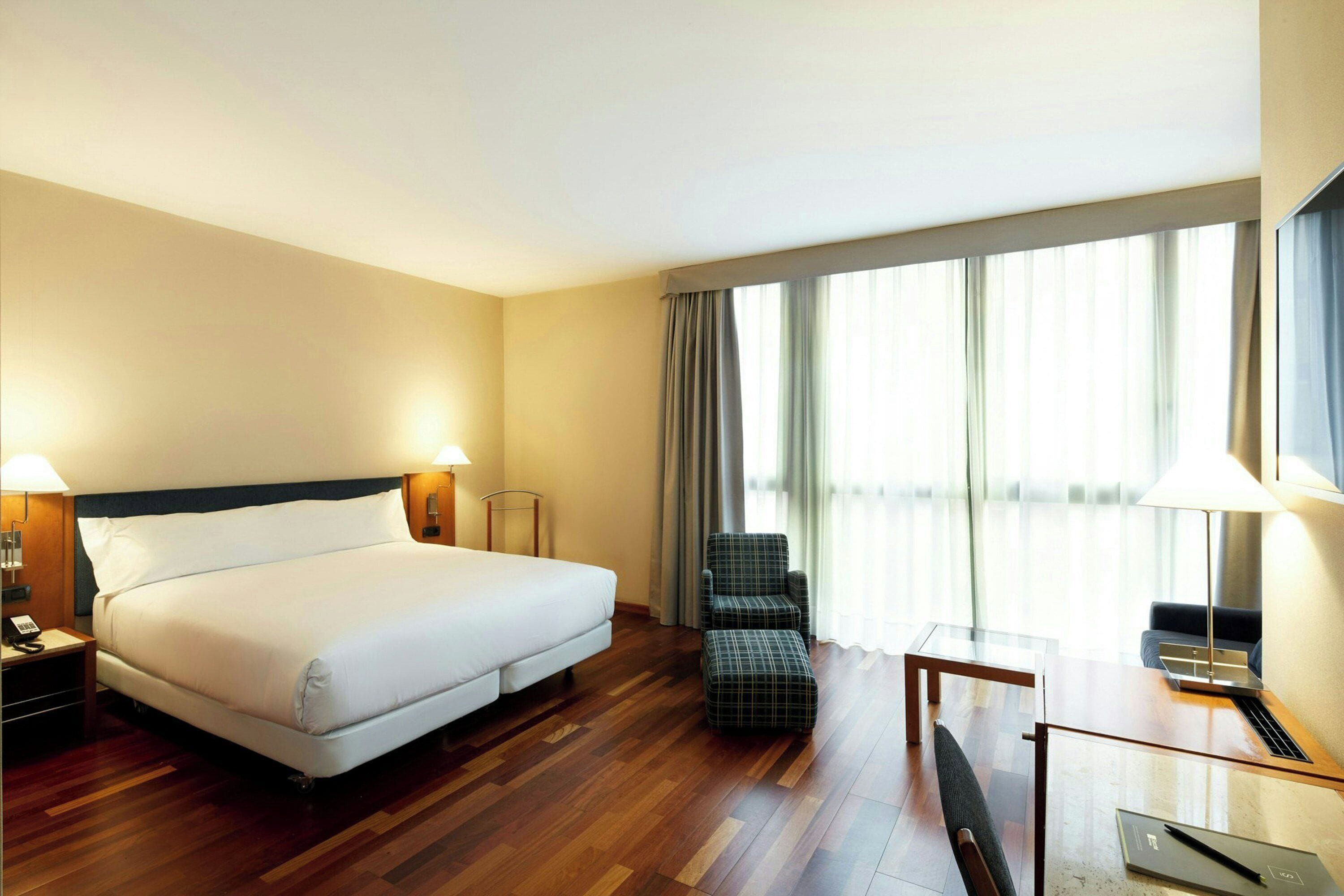 Habitación de hotel con una cama grande, un escritorio con silla, una mesita y un televisor.