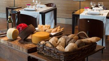 A wooden table with a variety of breads and cheeses, a bottle of wine, and a pepper mill.
