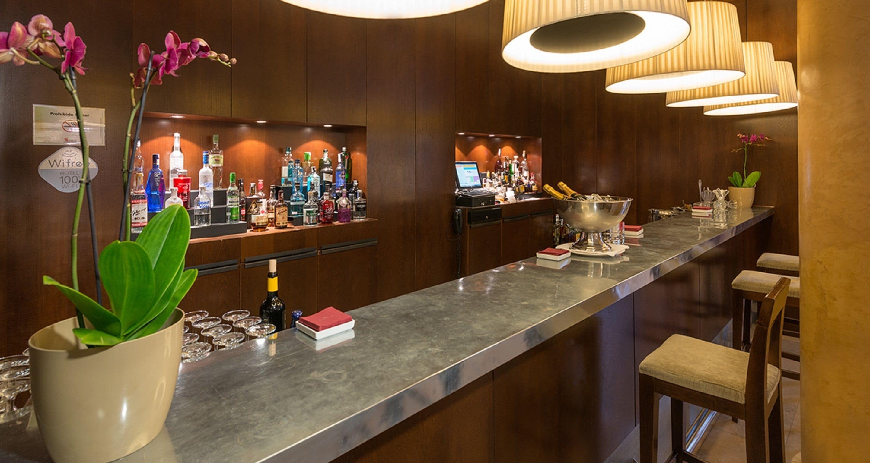 Una zona de bar con una barra larga, varias botellas y un ordenador portátil.