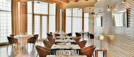 A dining area with multiple tables set for dining, large windows, and wooden paneling on the walls.
