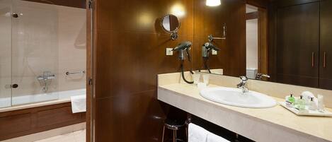 Un baño moderno con ducha de vidrio, un espejo grande y tocador con lavamanos y artículos de aseo.