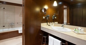 Un baño moderno con ducha de vidrio, un espejo grande y tocador con lavamanos y artículos de aseo.