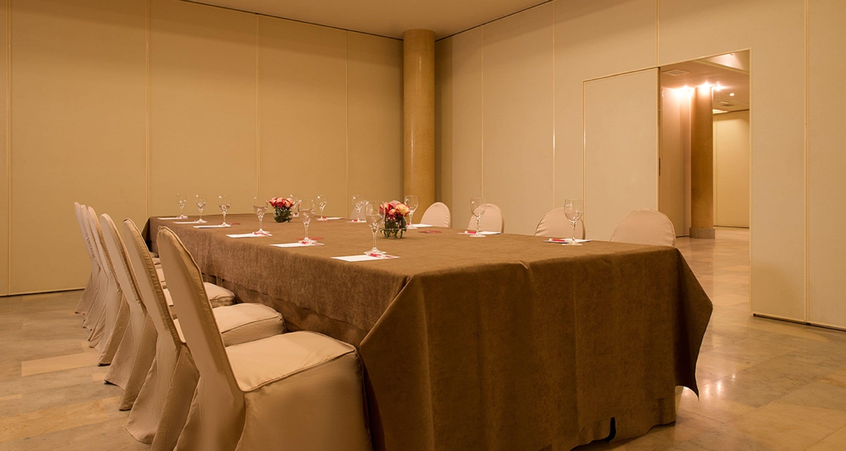 Un salón de conferencias con una larga mesa, sillas y centros de mesa florales.