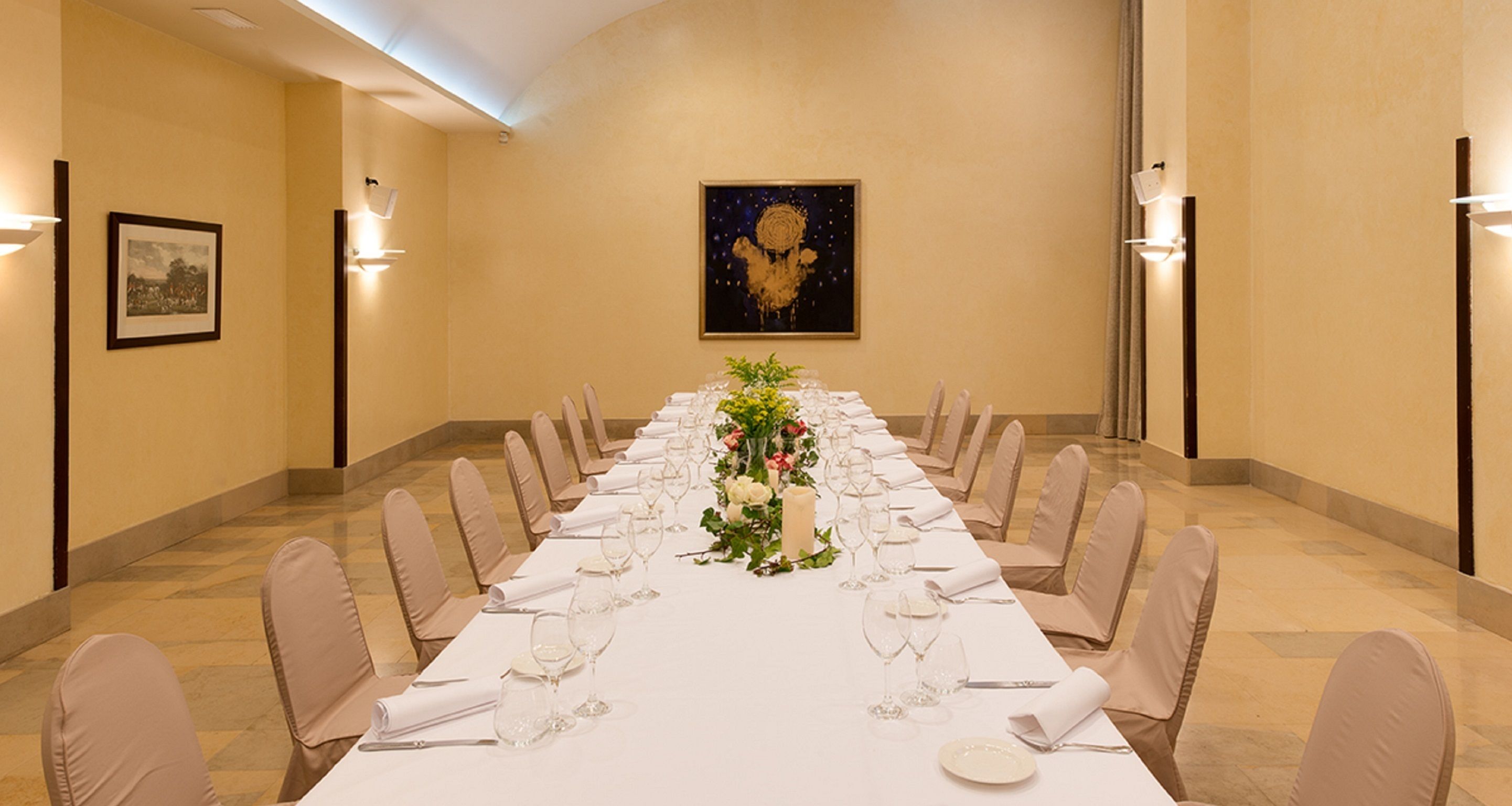 A long dining table set for a formal event with chairs, a floral centerpiece, and framed artwork on the walls.