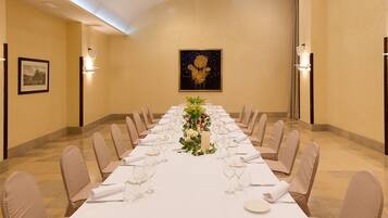 Une longue table à manger, dressée pour un événement formel, avec des chaises, un centre de table floral et des œuvres d’art encadrées accrochées aux murs.