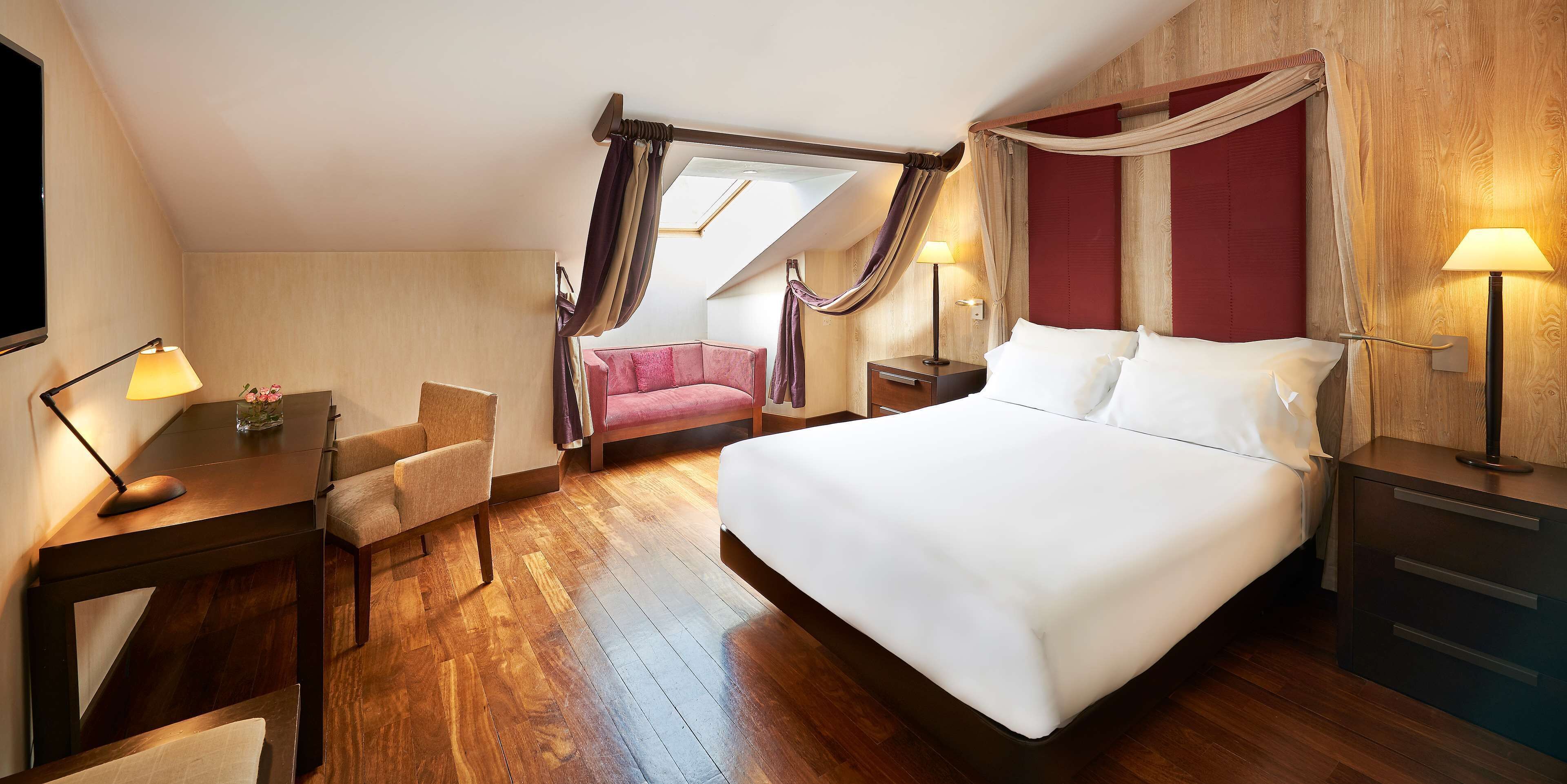 Habitación de hotel con una cama grande, un escritorio con lámpara, una silla y una mesita con un florero.