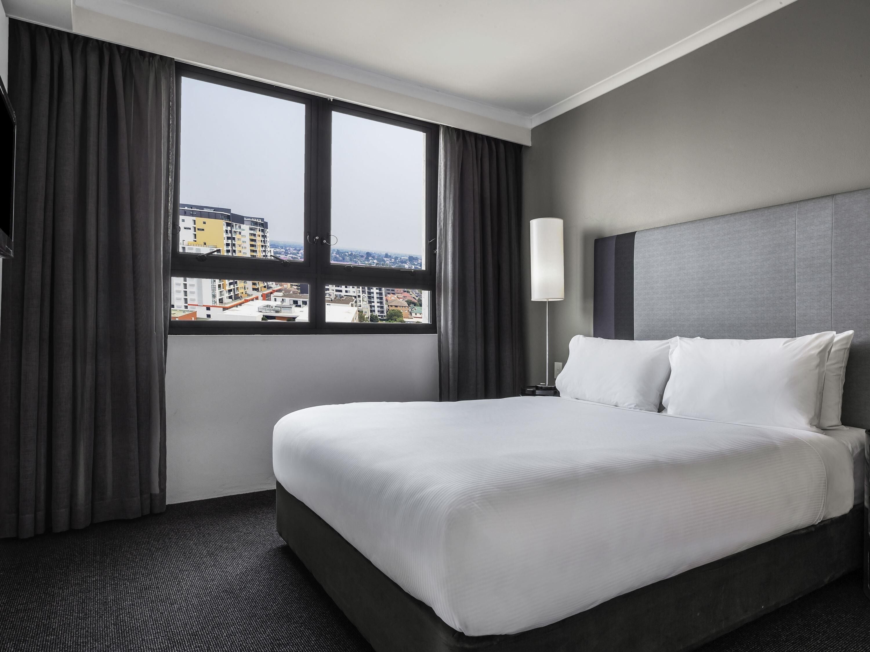 A hotel room with a large bed, a nightstand, a lamp, and a window with curtains.