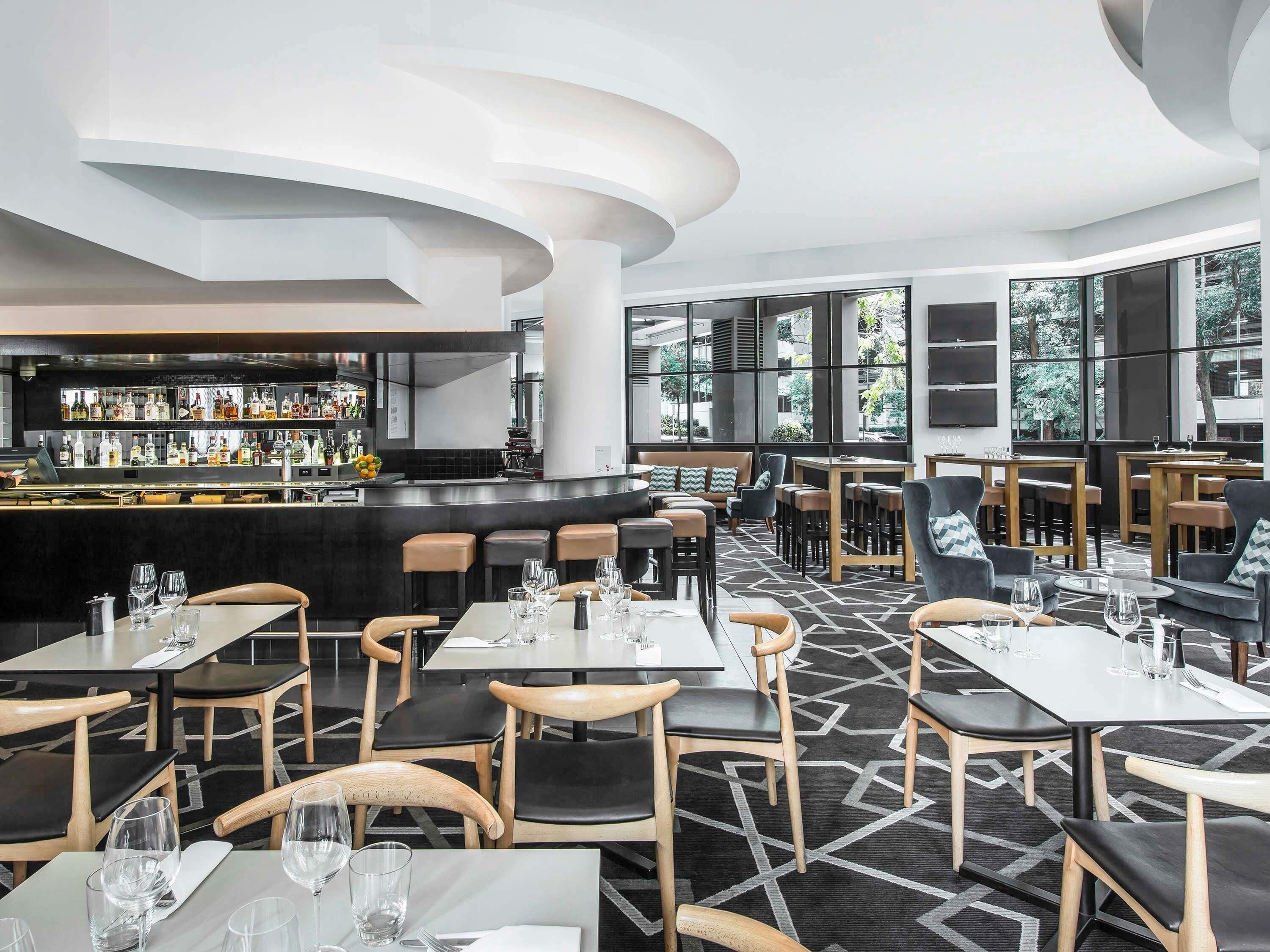 Un restaurante moderno con barra, diversas opciones de asientos y amplios ventanales que ofrecen vistas.