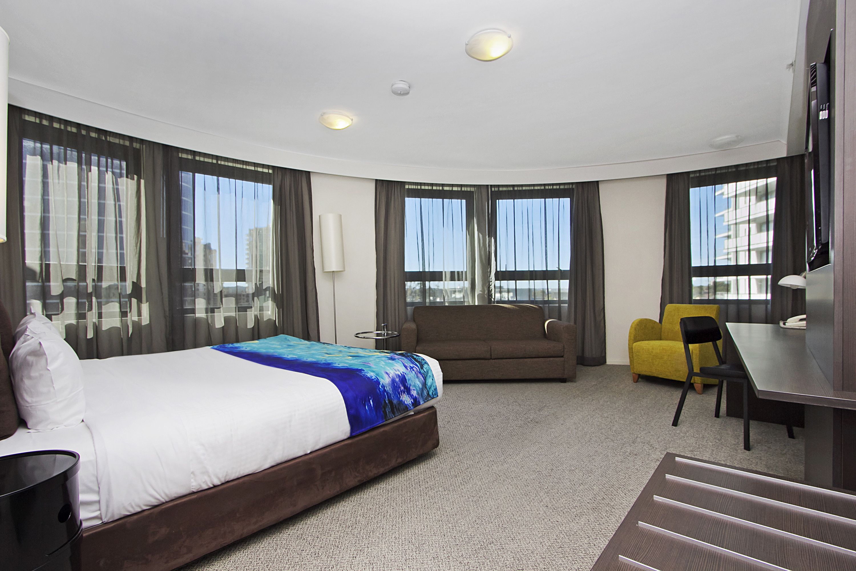 A hotel room with a bed, a sofa, a desk, and a chair.
