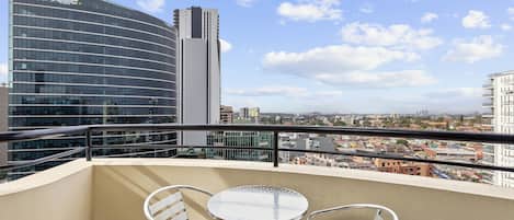 Un balcón con una mesa redonda y dos sillas, con vistas a un paisaje urbano con edificios modernos, incluido un edificio alto con la señalización 'Delotte'.