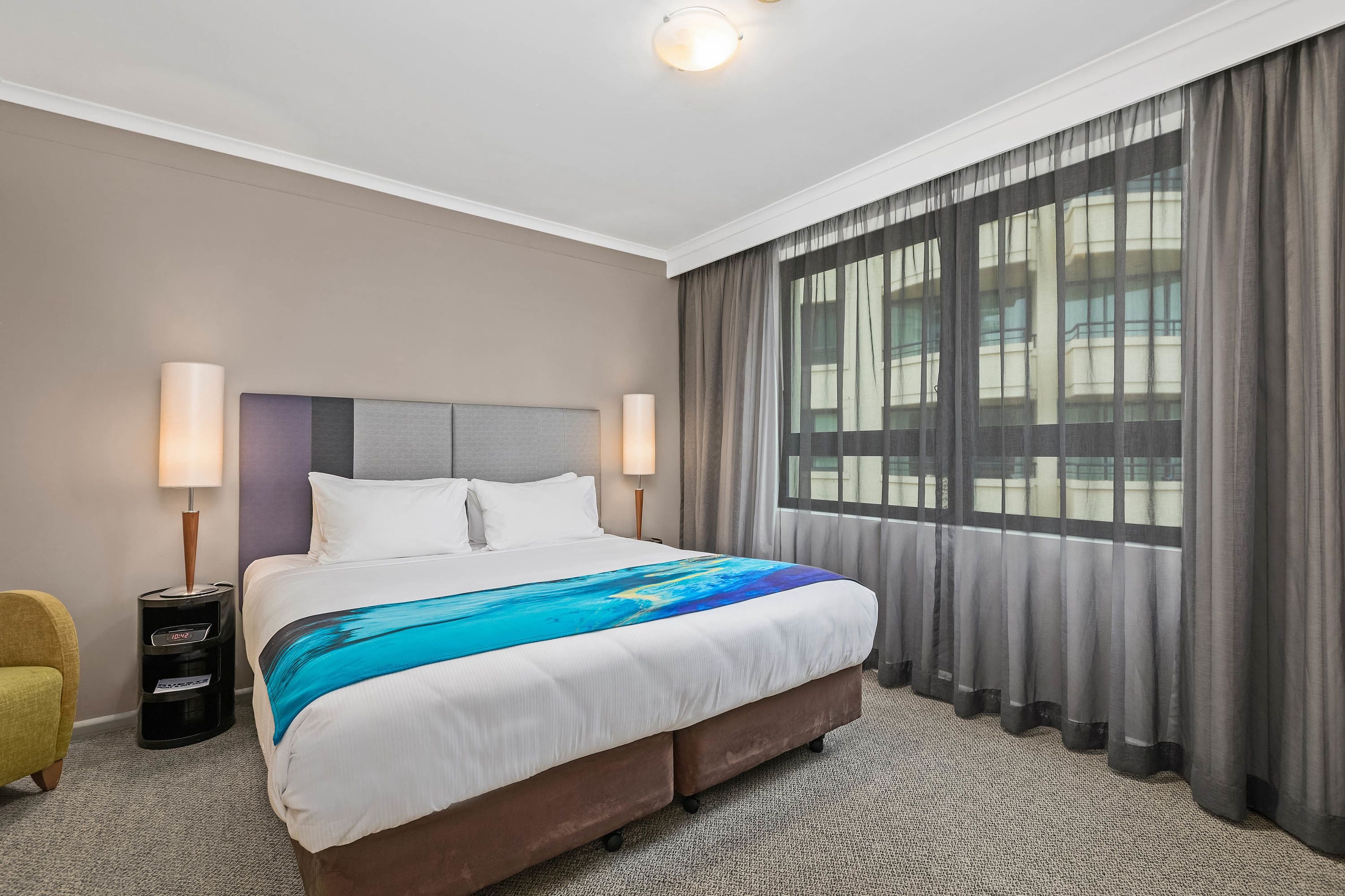 Una habitación de hotel con una cama grande, dos lámparas de noche, una silla y una ventana con cortinas.