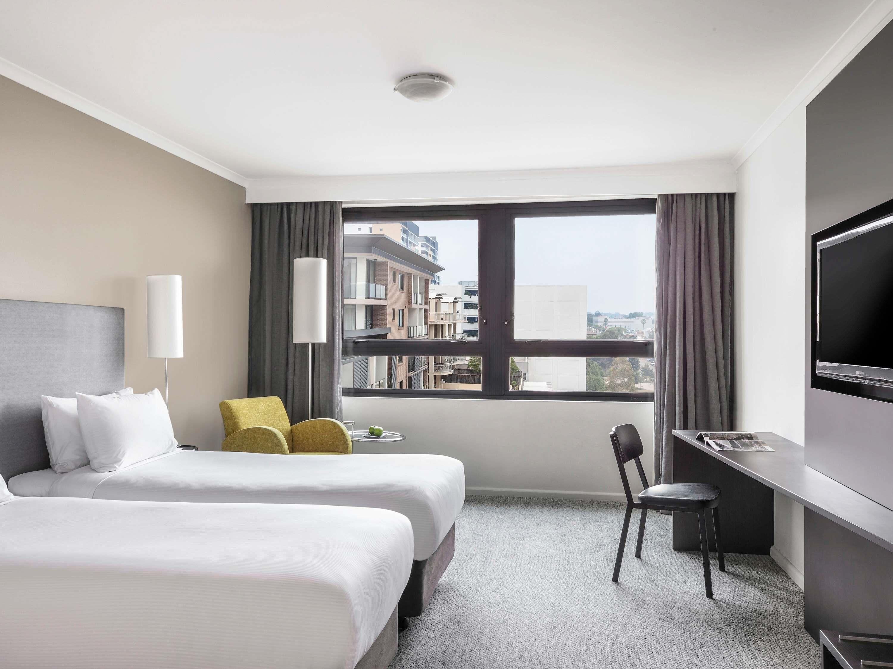 Habitación de hotel con cama, escritorio, silla, televisión y ventana con vista a la ciudad.