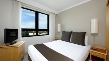 A hotel room with a large bed, a television on a wooden dresser, a window with curtains, and two bedside lamps.