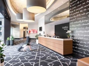 Un área de recepción moderna con una alfombra de estampado geométrico, un mostrador de recepción y una pared con citas inspiradoras.
