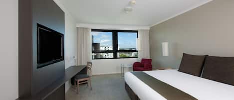 Camera d'albergo con un letto grande, una scrivania con una sedia, una TV a muro e una finestra con vista sulla città.