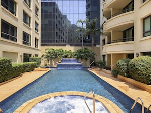 Una piscina con hidromasaje, rodeada de vegetación y edificios modernos.