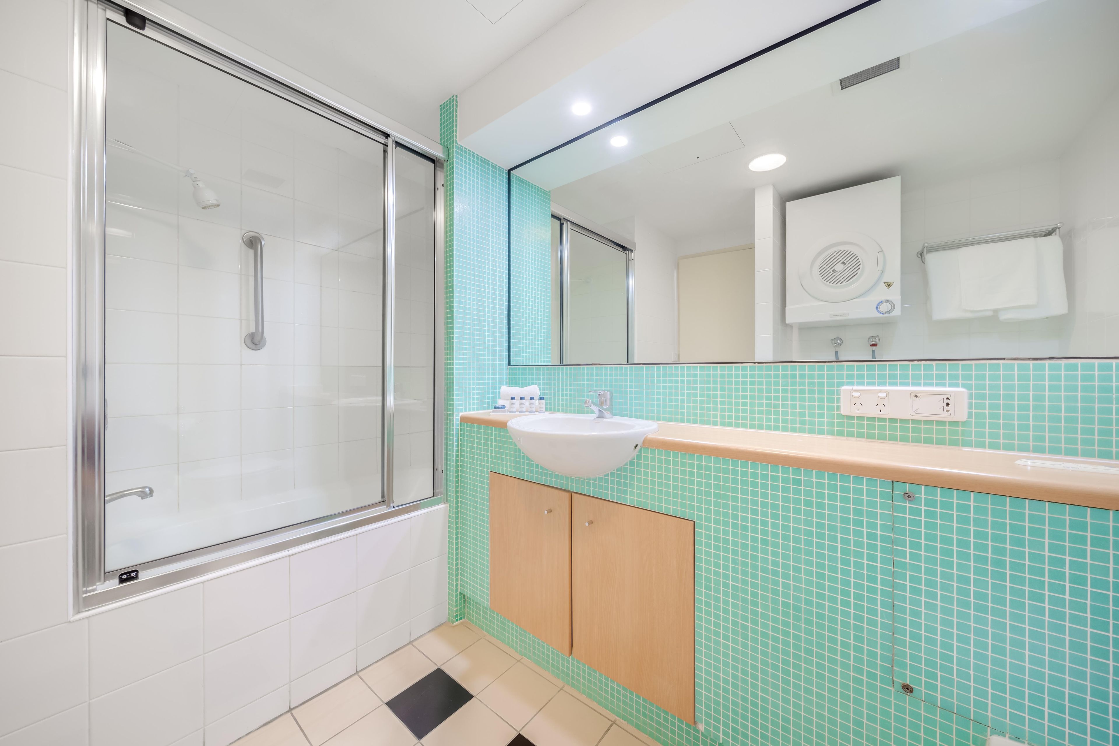 A bathroom with a glass shower enclosure, a sink with a mirror above it, and a tiled backsplash.
