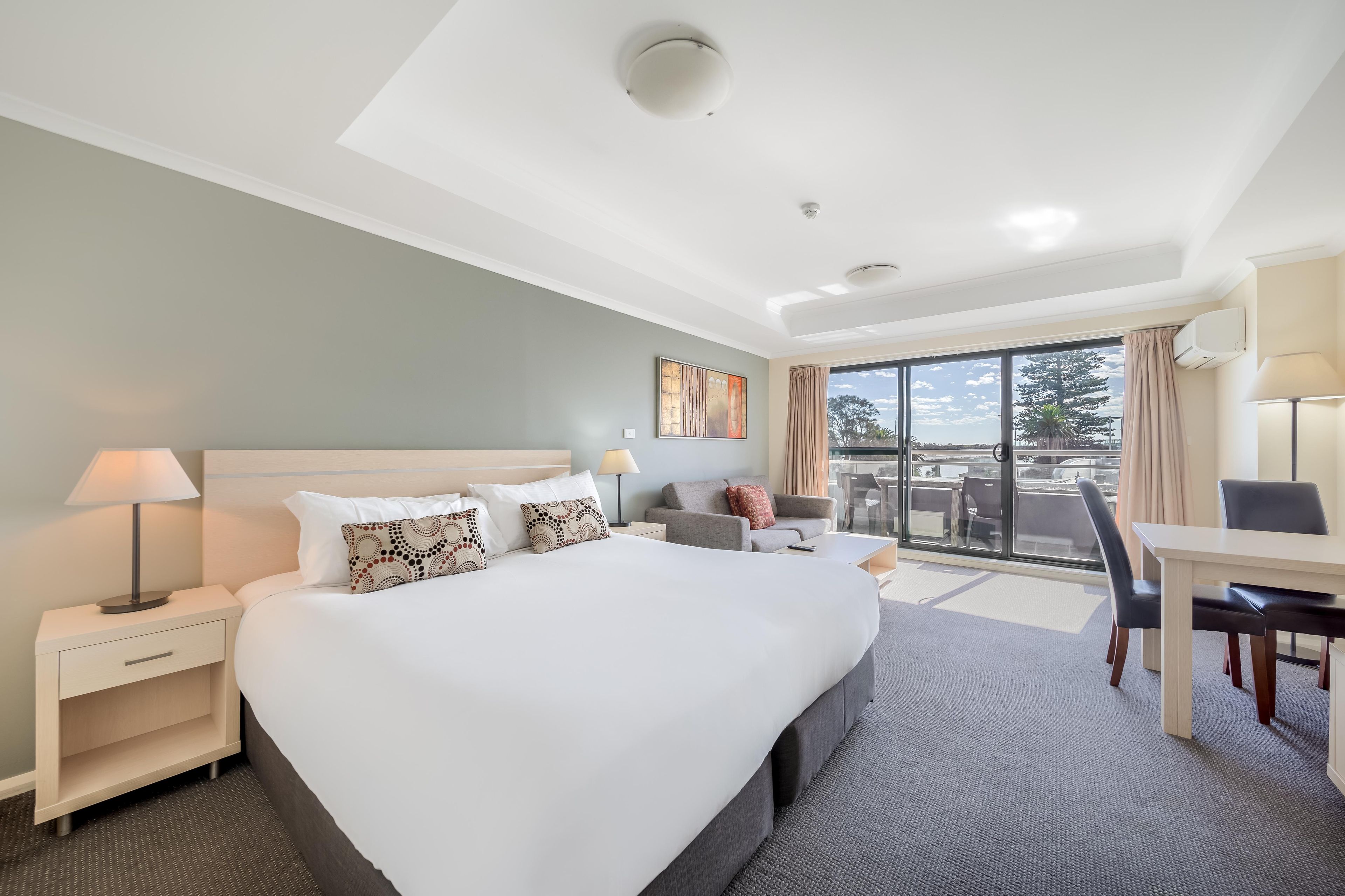A hotel room with a large bed, a desk, and a view of the outdoors.