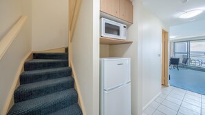 Eine Treppe mit gemustertem Teppich, ein weißer Kühlschrank und eine Mikrowelle auf einem Holzregal.