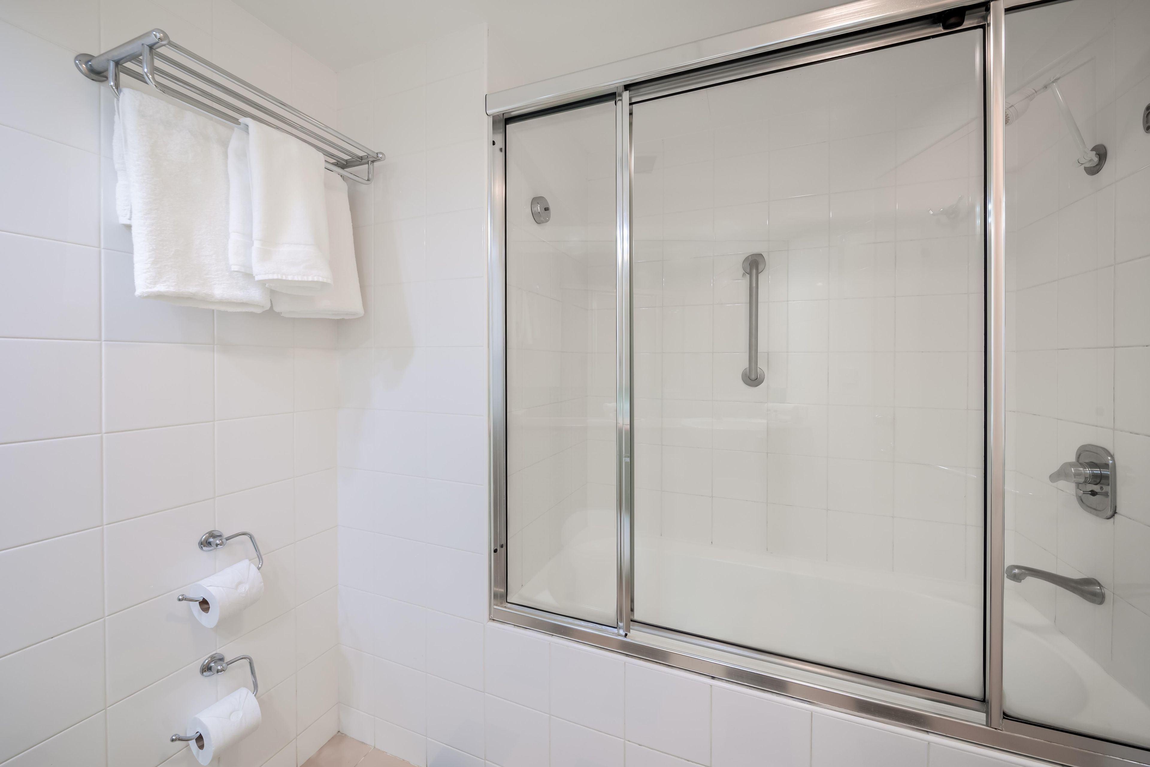 A bathroom with a glass-enclosed shower, white tiles, and a towel rack with folded towels.