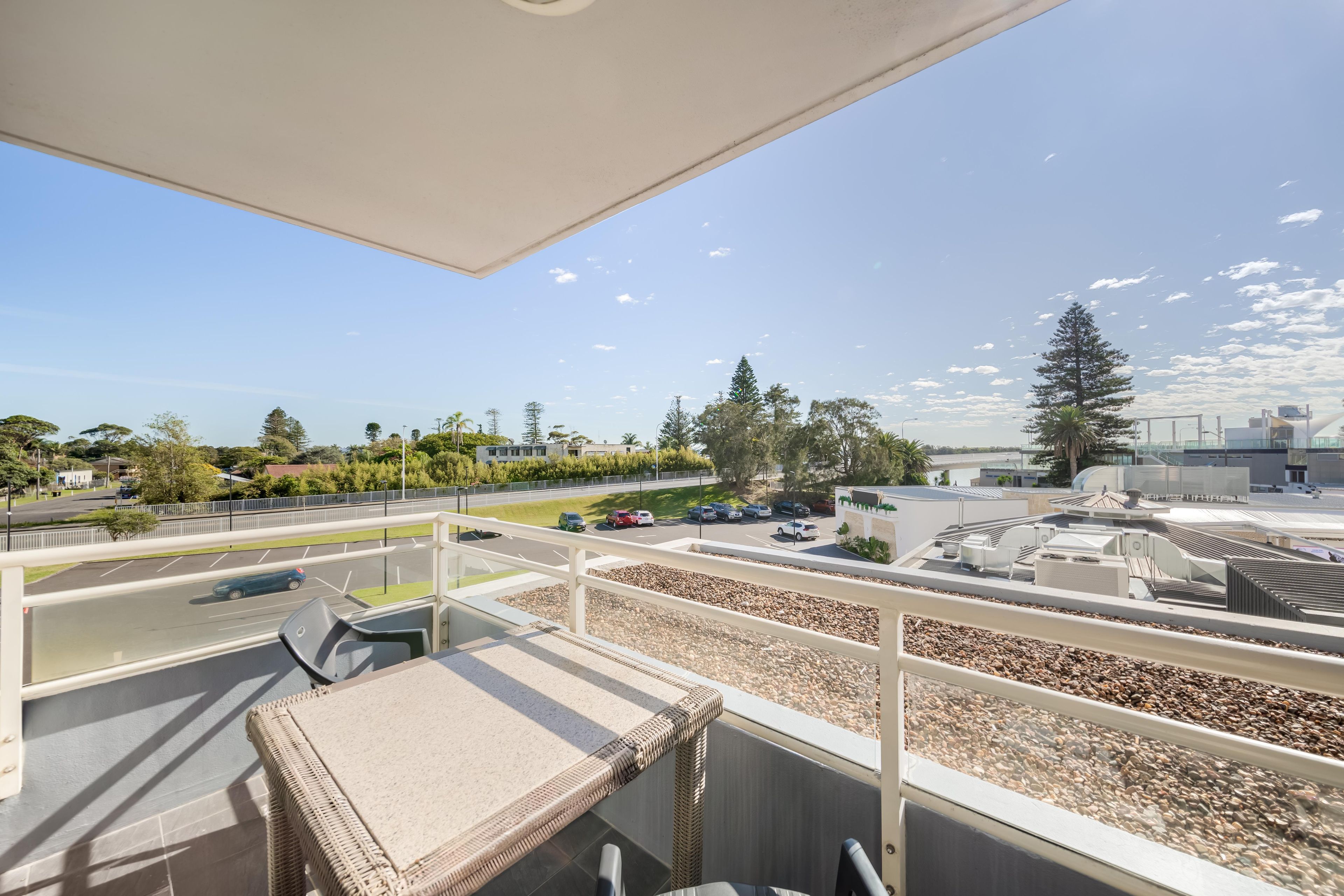 A balcony with a view of a parking lot and surrounding greenery.