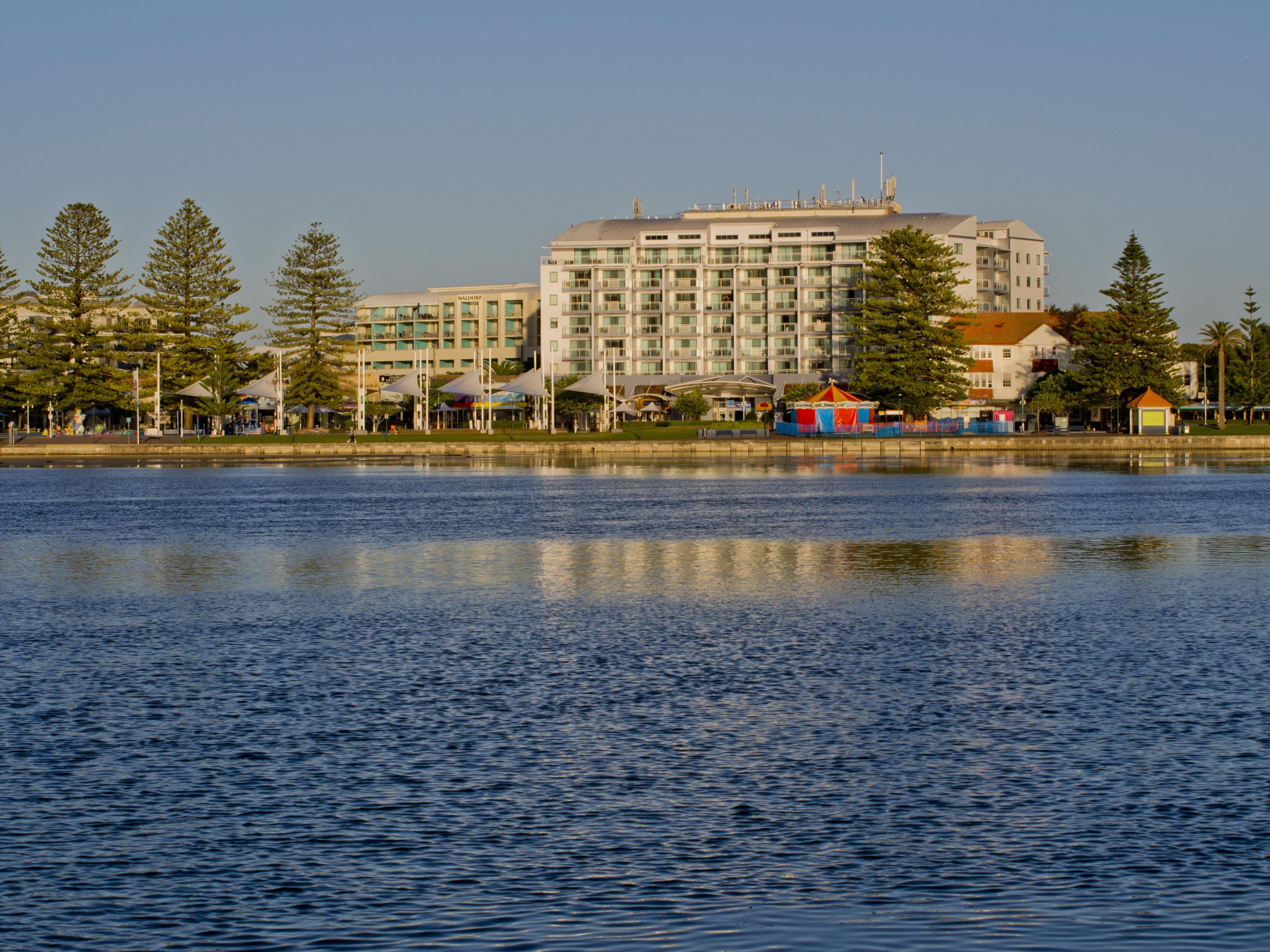 A waterfront hotel with a large building, a lake in the foreground, and trees around.