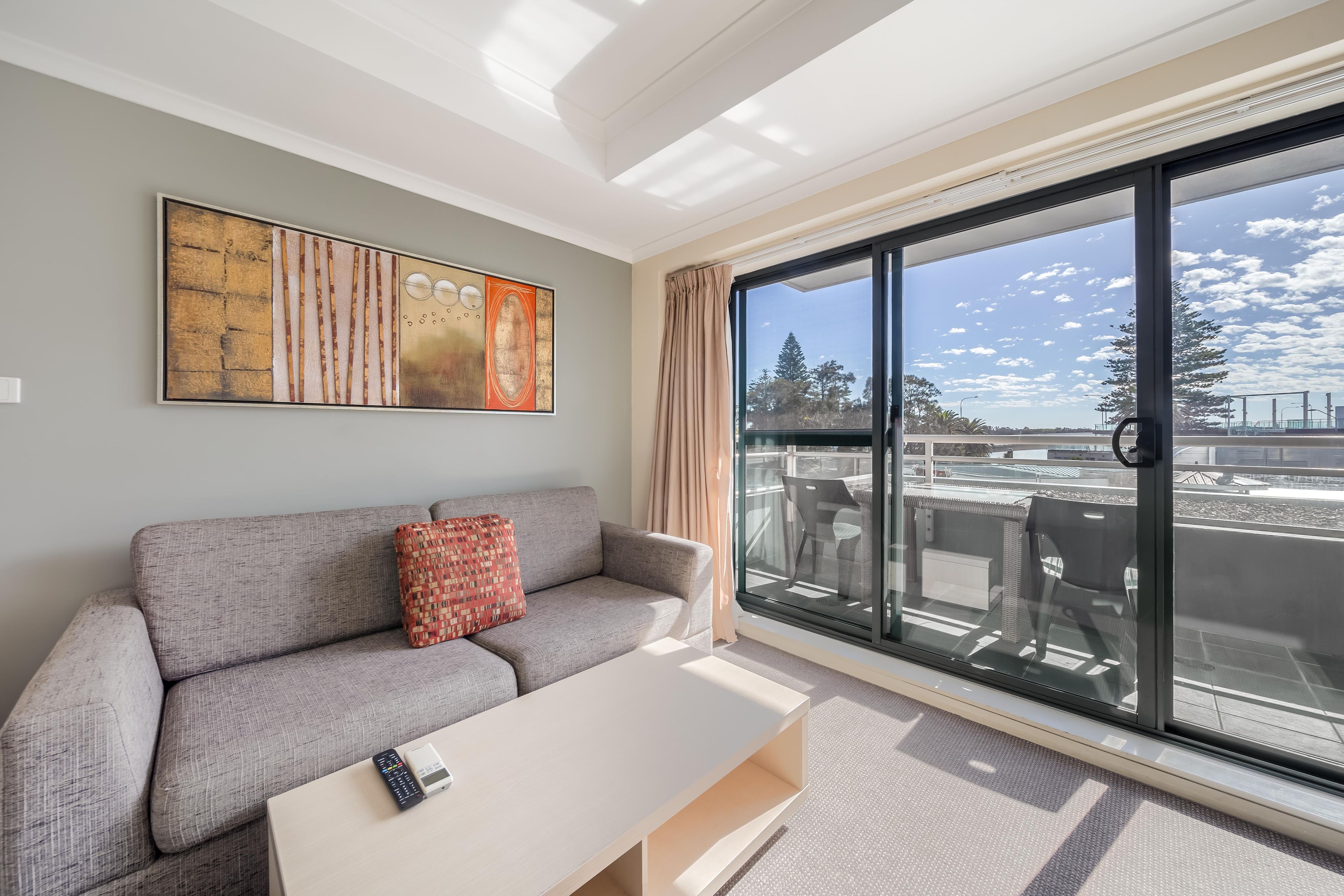 A modern living room with a grey sofa, a coffee table, and a large window with a view of the city.