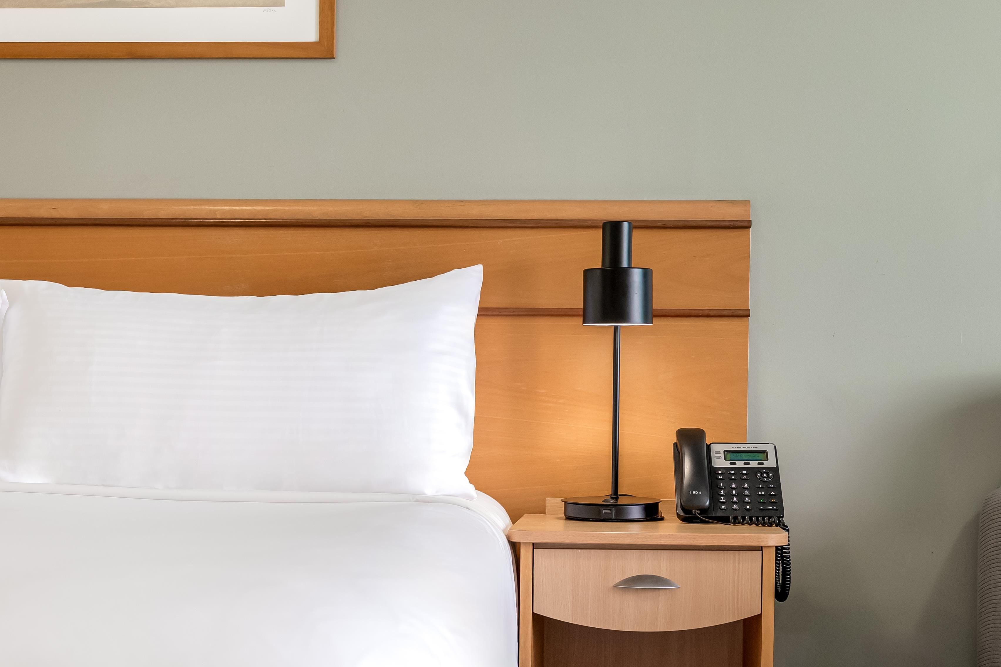 Ett hotellrum med en säng, ett nattduksbord, en lampa och en telefon.