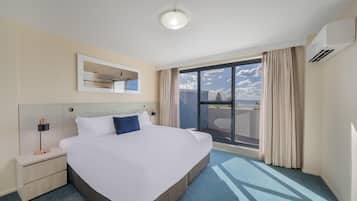 Habitación de hotel con una cama grande, una mesita de noche, una lámpara, una luz en el techo, una ventana con cortinas y un equipo de aire acondicionado.