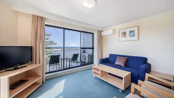 A hotel room with a large window, a flat-screen TV, a blue sofa, and a small wooden table.